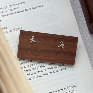 Minimalist S999 silver fishtail stud earrings with zircon on a dark wood display