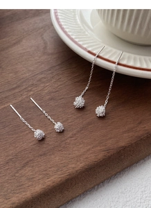 Macro detail of S925 sterling silver dandelion tassel earrings on wooden and ceramic decor