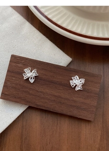Détail des boucles d'oreilles nœud en argent ajouré sur un support en bois texturé