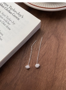 Detail view of silver dandelion tassel drop earrings on a dark wood grain table