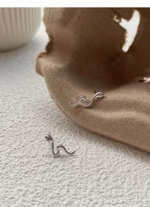 Dettaglio macro di orecchini a serpente in argento con zirconi su sfondo artistico
