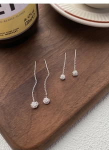 Detailed view of S925 sterling silver dandelion tassel earrings on a wooden tray