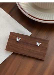 Close-up of minimalist silver butterfly stud earrings on a dark wood display stand