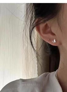 Close-up of a delicate 999 sterling silver butterfly stud earring and minimalist dot earring