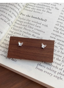 Detailed close-up of 999 sterling silver butterfly stud earrings on a wood board