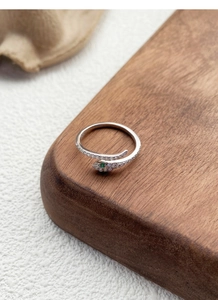 Detail of silver snake ring with white zircons and green eyes on textured surface