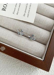 Macro shot of silver snake stud earrings with colorful cubic zirconia on a beige box