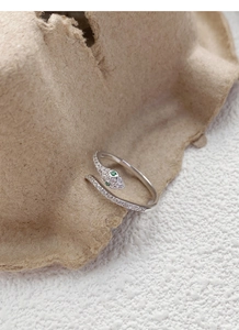 Macro shot of silver snake ring with white crystals and sparkling green gemstone eyes