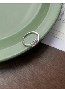 Detailed view of silver snake ring with green stone eyes and pave-set zircons on a tray