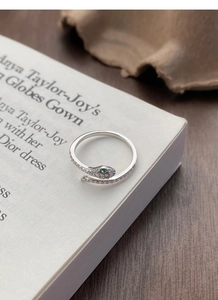 Macro detail of silver snake ring featuring green gem eyes and micro-paved zircons