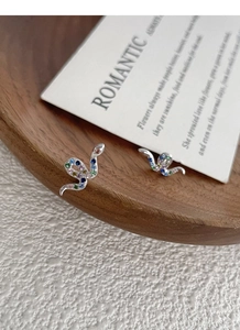 Macro shot of silver snake earrings with colorful zircon stones on a wooden tray