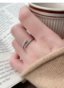 Detailed close-up of a silver snake ring with white zircons and green gem eyes worn on a hand