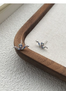 Macro shot of S925 silver snake stud earrings with colorful zircon stones on wooden tray