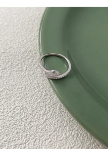 Detailed macro shot of a silver snake ring featuring green gem eyes and pavé white zircons