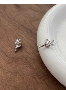 Macro detail of S925 silver snake stud earrings with zircon stone on wooden and ceramic surface
