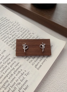 Macro shot of silver snake-shaped stud earrings with diamonds on a wooden display stand