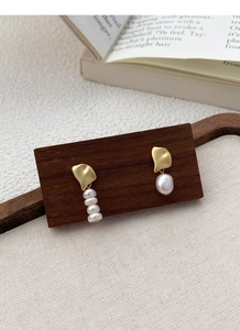 Detail of asymmetrical S925 silver earrings with baroque pearls on a wooden display