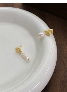 Close-up of asymmetric S925 silver earrings with baroque pearls on a white plate