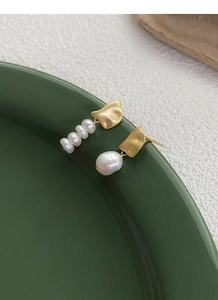 Detailed macro of asymmetrical S925 silver gold-plated baroque pearl earrings on ceramic