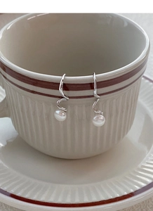 Detailed macro of spiral S925 silver pearl drop earrings hanging on a vintage cream ceramic cup