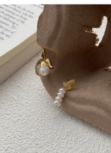 Artistic close-up of asymmetric S925 silver baroque pearl earrings on vintage paper background