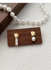Detail of asymmetrical S925 silver pearl earrings with gold leaf-shaped metal on wood