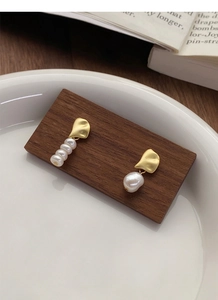 Detailed close-up of asymmetrical S925 silver pearl earrings on a wooden display stand