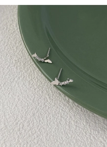 Gros plan de boucles d'oreilles papillon en argent avec zircons sur un plateau en céramique