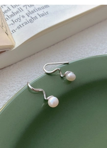 Elegant S925 silver wavy pearl drop earrings displayed on a dark green ceramic plate