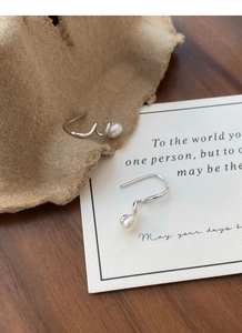 Macro shot of S925 sterling silver spiral earrings with elegant freshwater pearls on wood
