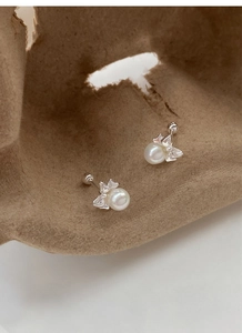 Close-up of pearl butterfly stud earrings with screw backs on textured paper