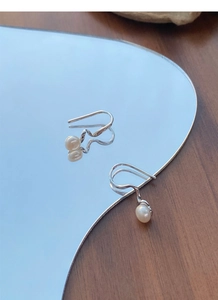 Detailed close-up of S925 silver spiral pearl earrings reflecting on a mirror surface
