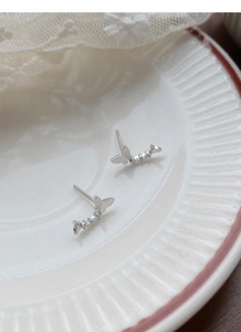 Gros plan de boucles d'oreilles papillon en argent 999 et strass sur une assiette blanche
