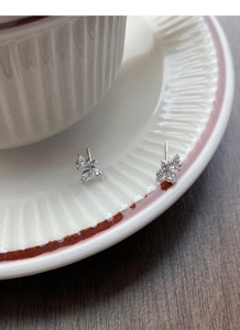 Dettaglio di orecchini a lobo in argento con zirconi appoggiati sul bordo di una tazza