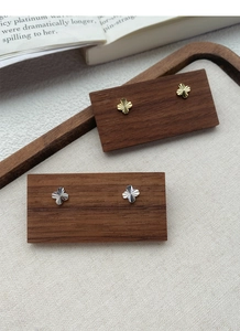 Detailed view of silver and gold clover earrings with radial texture on a wooden stand