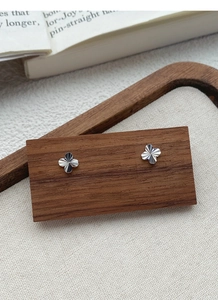 Macro detail of silver four-leaf clover stud earrings with textured radial engravings