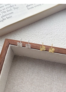 Close-up of gold and silver clover earrings with radiant textured finish on wood