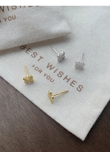 Macro shot of silver and gold clover earrings with S925 hallmark on a linen pouch
