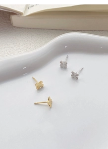 Detail of clover earrings in gold and silver with radial texture on a white plate