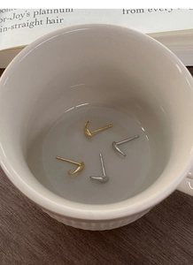 Minimalistische gebogene Hakenohrringe in Gold und Silber auf einer Keramiktasse