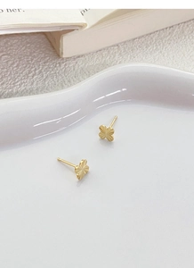 Detail of gold four-leaf clover earrings with radial texture on white ceramic plate