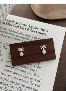 Close-up of S999 silver bow pearl earrings displayed on vintage book background