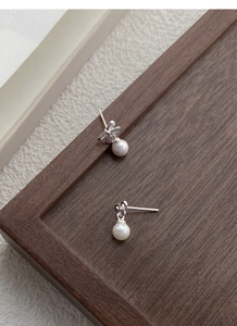 Close-up of S999 sterling silver bow earrings with round white pearls on a wood tray