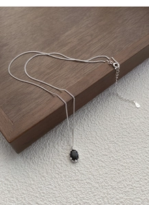 Close-up of S925 sterling silver chain with black oval zircon pendant on wood