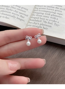 Close-up of elegant silver bow pearl earrings held by hand over a vintage book background