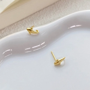 Elegante goldene Delfin-Ohrstecker aus S999 Sterlingsilber auf einem weißen Keramiktablett