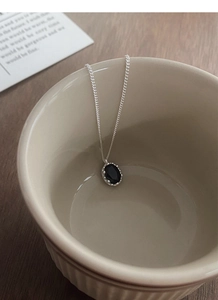 Close-up of a 925 sterling silver oval black zircon pendant necklace in a ceramic bowl
