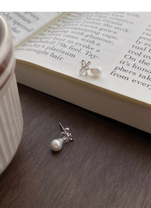 Macro detail of S999 silver bowknot earrings with white pearls on a vintage book page