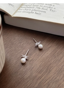 Detailed view of silver bow-shaped pearl stud earrings on a vintage wood texture