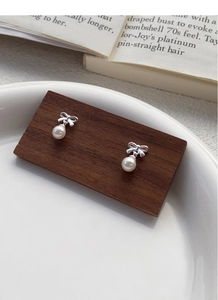 Detail of silver bow pearl earrings featuring glossy white pearls on a dark wood stand